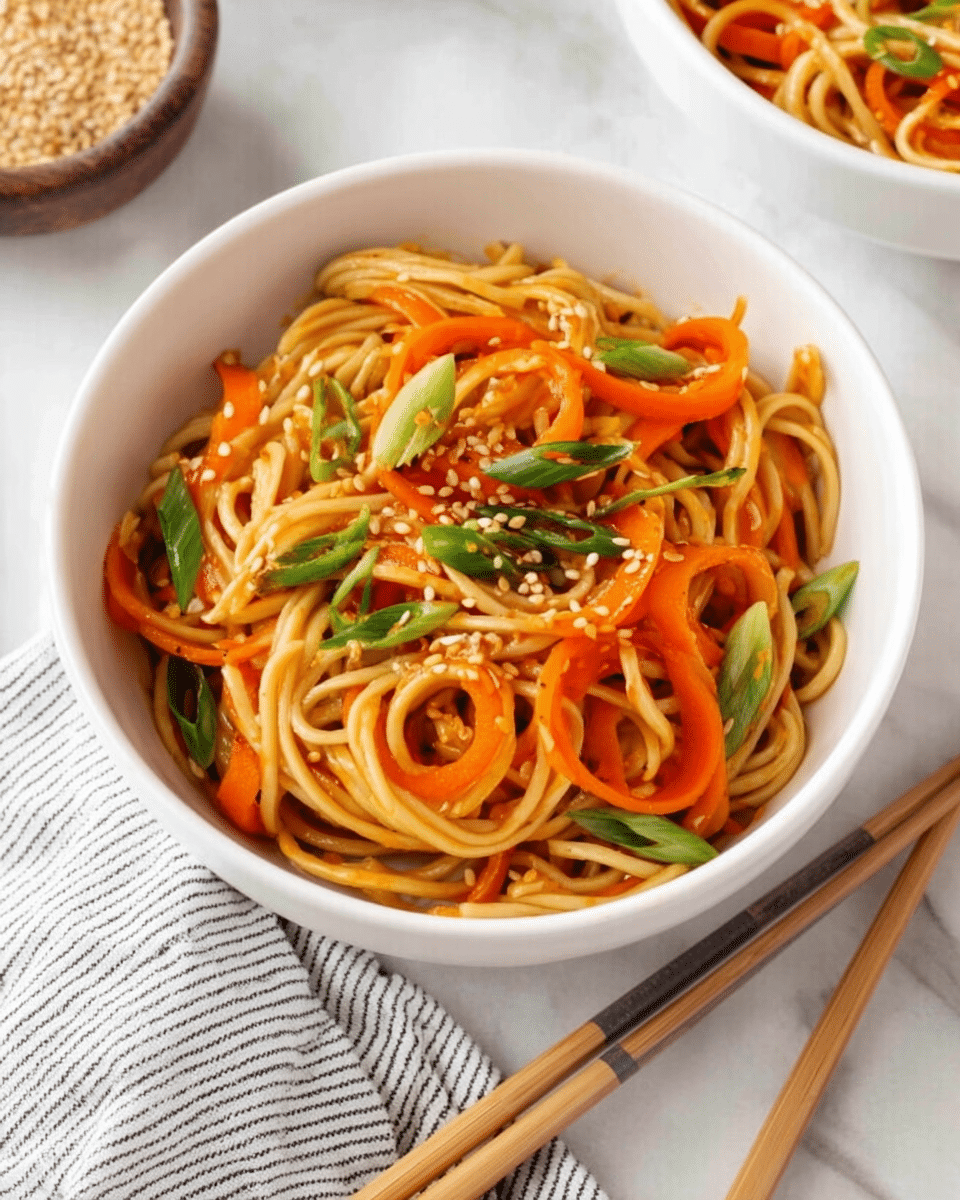 A white bowl filled with light golden noodles mixed with curled bright orange carrot slices, scattered green onion pieces, and light brown sesame seeds on top. The noodles look soft and slightly shiny. The bowl rests on a white marbled surface next to a pair of wooden chopsticks with gray handles. There is a small white bowl of sesame seeds and a small white bowl of green onion slices around the main bowl, with a white and black striped cloth partially visible in the upper right corner. Photo taken with an iphone --ar 4:5 --v 7