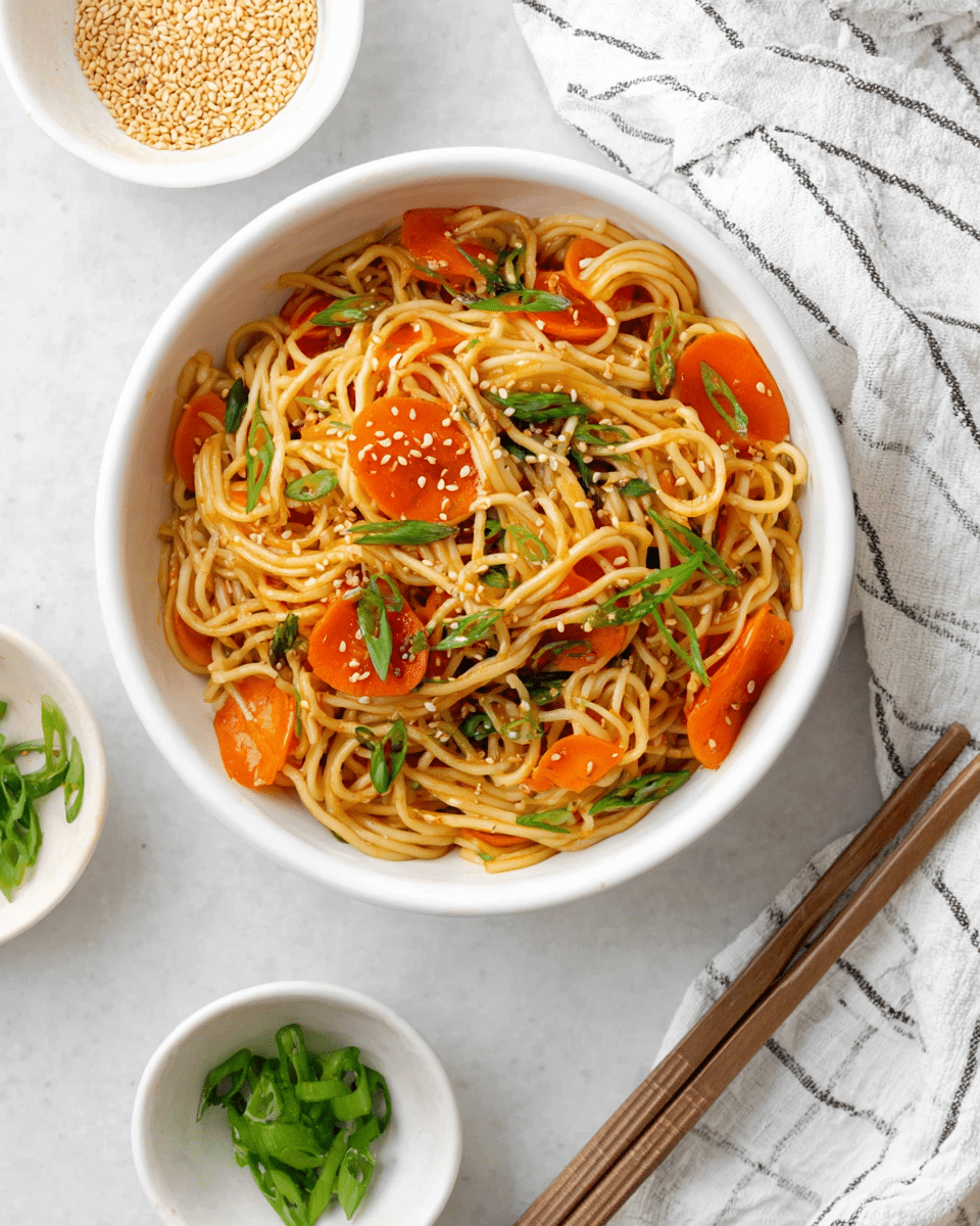 A white bowl filled with light brown cooked noodles mixed with bright orange carrot rings. Scattered on top are fresh green slices of spring onions and light beige sesame seeds. The bowl is placed on a white marbled surface with a striped cloth nearby. A pair of wooden chopsticks with gray tips lies in front of the bowl. A small part of another bowl with similar contents is visible in the top left corner. Photo taken with an iphone --ar 4:5 --v 7