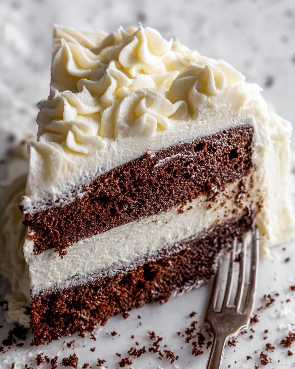 A close-up view of a slice of two-layer chocolate cake with thick white frosting between the dark brown layers and on top. The frosting is thick and smooth, with some swirls and peaks, covering the sides and top of the slice. The slice is held by a fork on the right side, resting on a white marbled surface with small brown crumbs scattered around. The rich texture of the cake contrasts with the creamy white frosting swirled around it. photo taken with an iphone --ar 4:5 --v 7