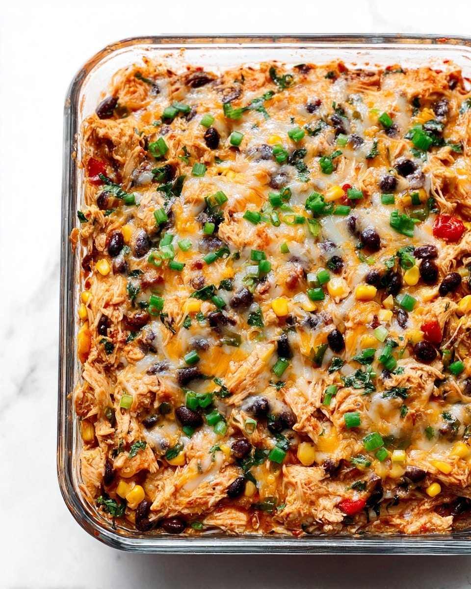 The dish is a colorful baked casserole in a clear glass square baking dish, filled with mixed layers of shredded chicken in reddish sauce, black beans, yellow corn, and small diced red peppers, all mixed with melted cheese. The top layer shows a mix of golden melted cheese, scattered bright green chopped herbs and green onions, alongside whole black beans and visible pieces of chicken and corn, creating a textured, hearty look. The dish rests on a white marbled surface. photo taken with an iphone --ar 4:5 --v 7