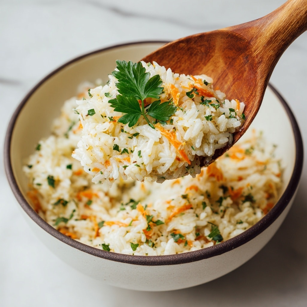 The image shows a close-up of a cooked rice dish inside a white pot with a wooden spoon lifting a scoop. The dish has about two main layers: white and yellowish cooked rice mixed evenly with shredded orange carrot bits and small green herb leaves scattered throughout. Pieces of tender light brown chicken are mixed inside the rice, giving texture and color contrast. The rice looks soft and fluffy, with some fresh green parsley leaves on top adding freshness. The background is a white marbled surface, creating a clean and bright setting. Photo taken with an iphone --ar 4:5 --v 7