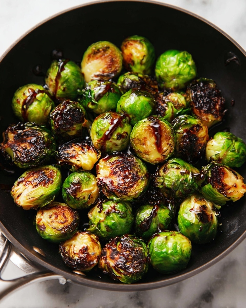 A black skillet filled with roasted Brussels sprouts that are browned and crispy on the outside, with a mix of vibrant green and charred dark brown colors, topped with scattered golden roasted almonds. The skillet sits on a white marbled surface, giving a clean and bright background, with a light drizzle of a dark glossy sauce spread unevenly across some sprouts. Small sprigs of green herbs are visible near the corner of the skillet, enhancing the fresh look. photo taken with an iphone --ar 4:5 --v 7