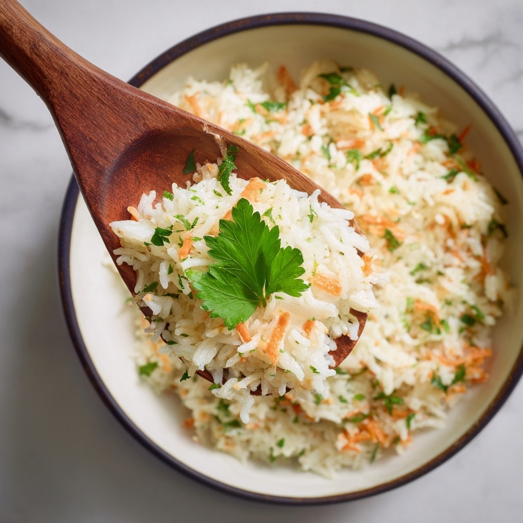 A close-up view of a wooden spoon lifting a creamy rice dish from a white bowl with a dark rim. The dish has three main layers: the soft rice grains that are off-white and slightly shiny, mixed with small orange shredded carrot pieces scattered throughout, and small green herbs sprinkled on top adding a fresh touch. At the very center, a single bright green leaf of parsley sits atop the rice on the spoon, making the dish look fresh and moist. The white bowl sits on a white marbled textured surface, creating a clean and bright background. photo taken with an iphone --ar 4:5 --v 7