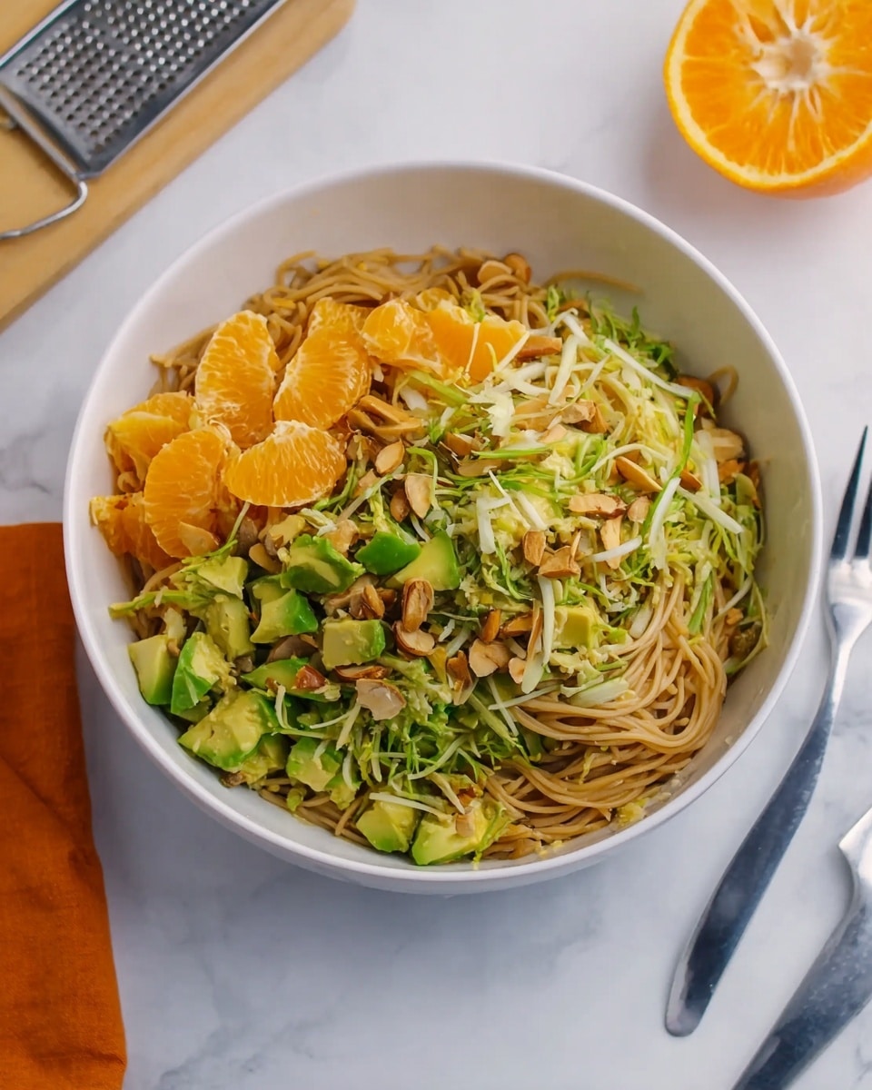 A white bowl filled with a noodle salad that has three main layers: at the bottom, thin light brown noodles form the base; the middle layer is made of small green avocado pieces and bright orange chunks of mandarin; the top layer is a mix of thin green strips, crunchy almond slices, and some small brown pieces, likely nuts or tofu, scattered around, all sitting on a white marbled surface with a fork next to the bowl and a grated utensil nearby, with a partly cut orange in the background. photo taken with an iphone --ar 4:5 --v 7