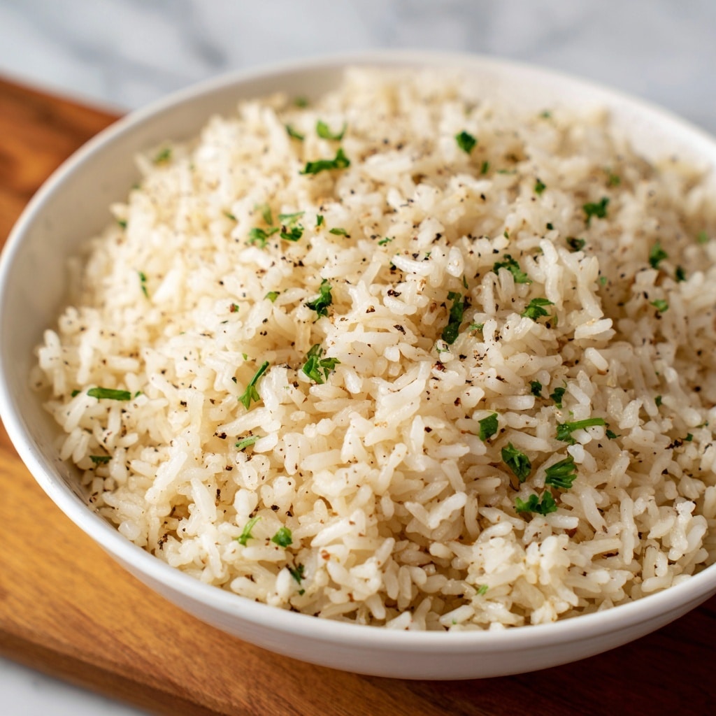 A close-up view of a white bowl filled with fluffy cooked rice, each grain separate and soft in texture. The rice is light beige in color with small black pepper specks and tiny green parsley bits scattered evenly throughout. The bowl sits on a wooden surface, but the background is changed to a white marbled texture for clarity. The dish shows no other layers, just the simple seasoned rice filling the bowl. Photo taken with an iphone --ar 4:5 --v 7