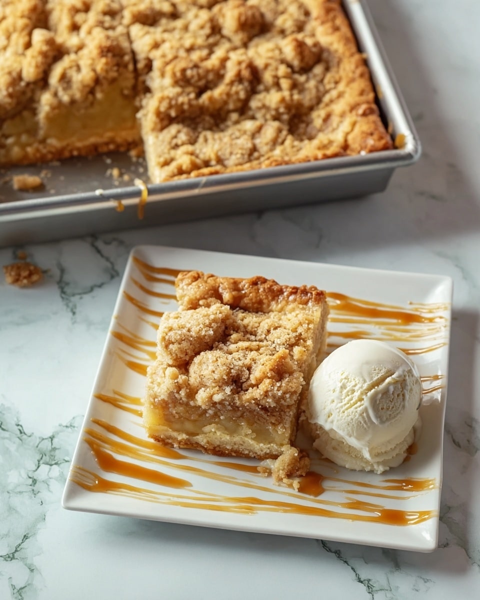 A white plate holds one square piece of crumb cake topped with a scoop of white ice cream and thin caramel strands draped lightly over the ice cream and cake. The crumb cake has three visible layers: a golden brown bottom crust, a middle layer of light brown cake with chunks of yellow fruit or filling, and a crumbly golden topping with a rough texture. Next to the plate is a metal baking tray with more pieces of the same crumb cake, showing the same layers and a slightly raised crust edge. The scene is set on a white marbled surface. Photo taken with an iphone --ar 4:5 --v 7