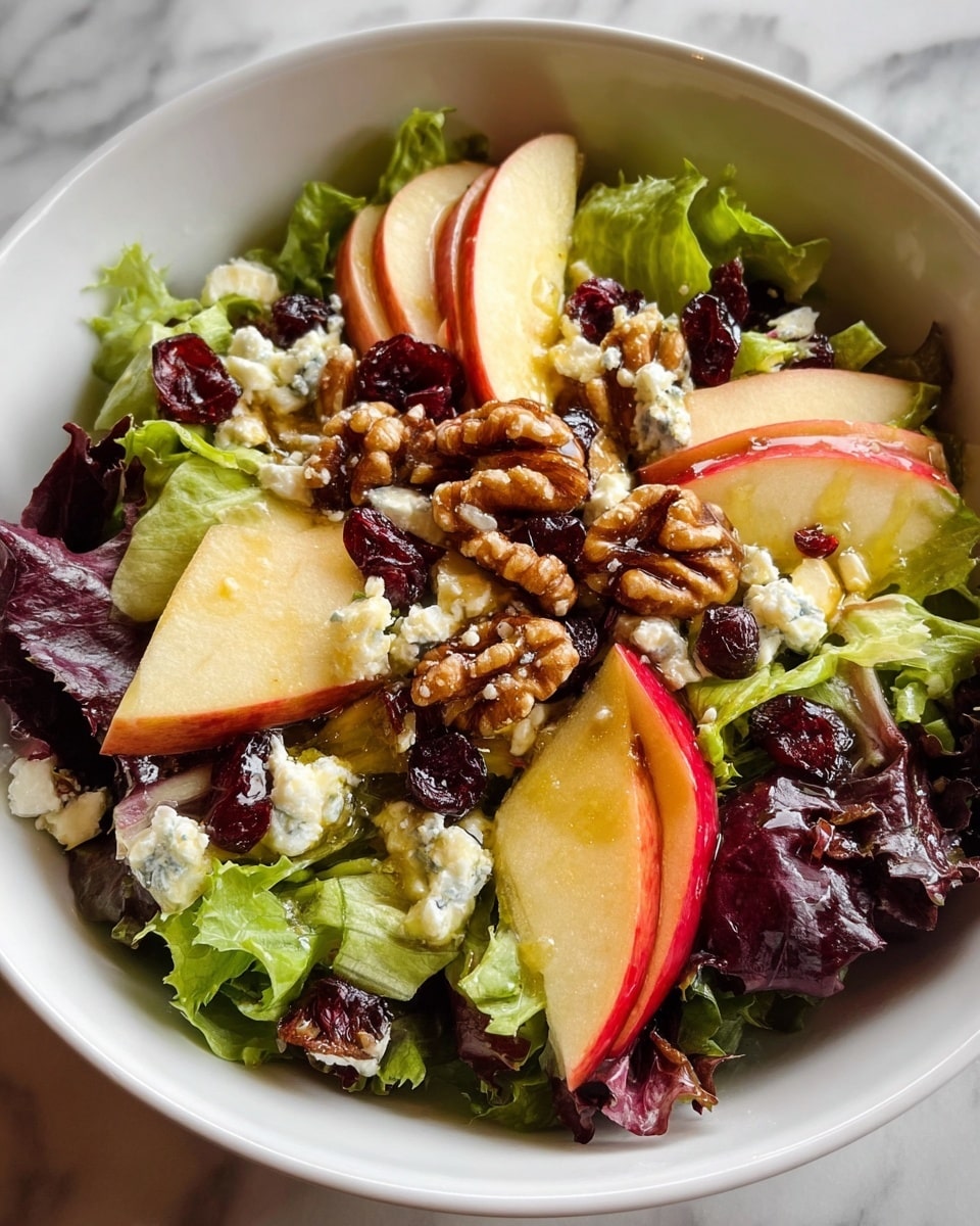 A white bowl filled with a fresh salad showing three main layers: the bottom layer is bright green leafy lettuce with a soft, ruffled texture, the middle layer has thin slices of red and yellow apple arranged in a circular pattern, and the top layer consists of crumbled white cheese, dark red dried cranberries, and golden brown walnut pieces scattered evenly over the salad. The bowl is placed on a white marbled surface with natural sunlight casting soft shadows, enhancing the colors and textures of the ingredients. Photo taken with an iphone --ar 4:5 --v 7