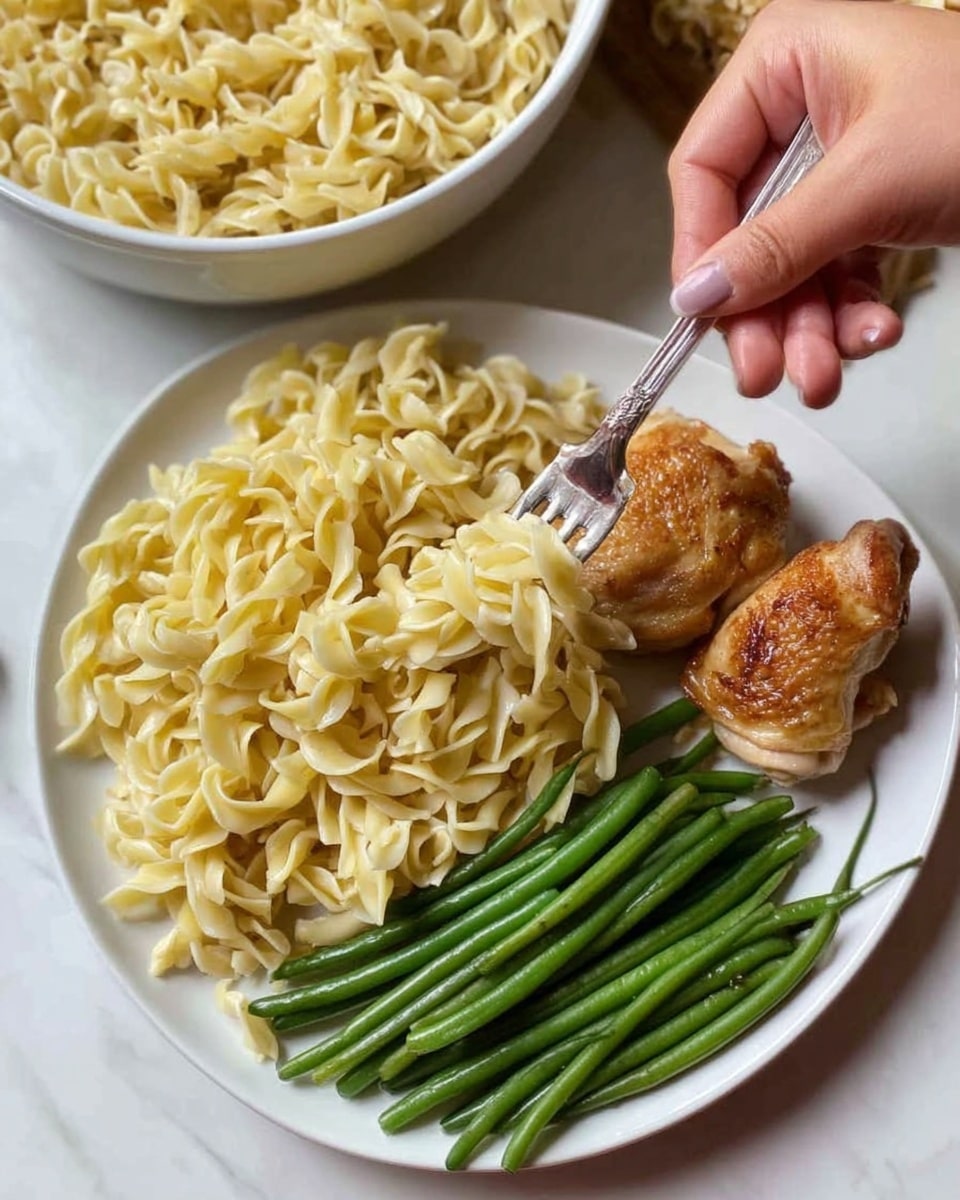 The image shows a square white bowl filled with light yellow, cooked egg noodles layered loosely with a few small slices of mushrooms mixed in. A woman's hand holding a spoon is reaching into the bowl from the top left corner, ready to scoop some noodles. The background surface is a white marbled texture, with some green and brown blurred objects around the bowl, giving a natural, fresh feel. The lighting is soft, highlighting the texture of the noodles and mushrooms. Photo taken with an iphone --ar 4:5 --v 7