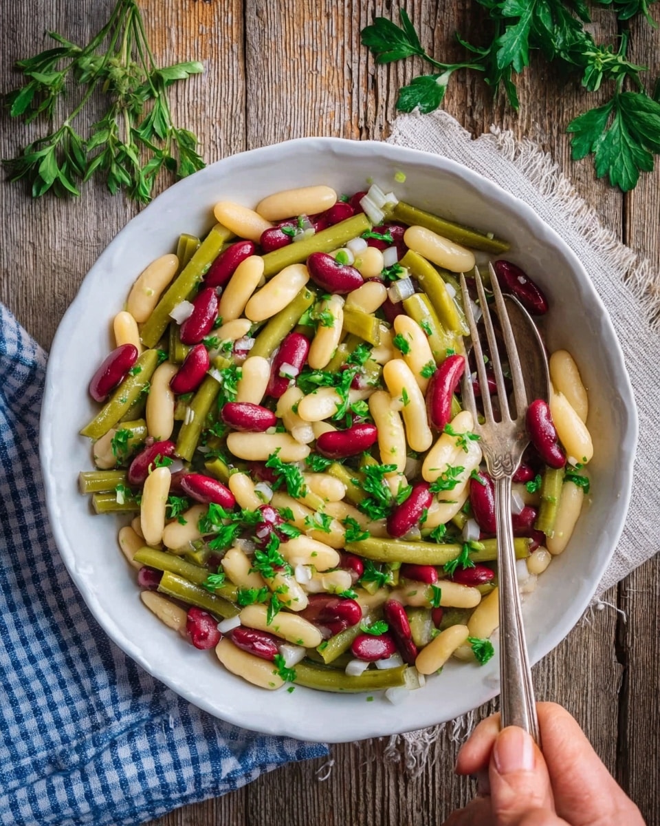 A clear glass bowl filled with a colorful salad made of cut green beans, red kidney beans, and finely chopped green herbs evenly mixed together, showing layers of long green bean pieces and bright red kidney beans. The texture of the beans looks soft but firm, garnished with small bits of fresh leafy herbs on top. The bowl is placed on a white marbled surface. photo taken with an iphone --ar 4:5 --v 7