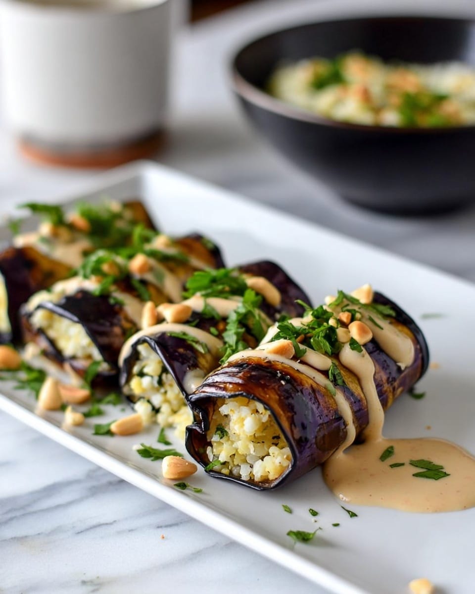 A white rectangular plate holds six pieces of grilled eggplant rolls arranged in a row. Each roll is made of thin grilled eggplant slices with visible brown grill marks wrapped around a light-colored grain and herb filling. The rolls are topped with a creamy white sauce drizzled in lines, fresh green chopped herbs, and pale beige pine nuts scattered over and around them. In the background, a black bowl with a wooden spoon contains more filling and a ceramic cup with sauce sits on a white marbled surface. Photo taken with an iphone --ar 4:5 --v 7
