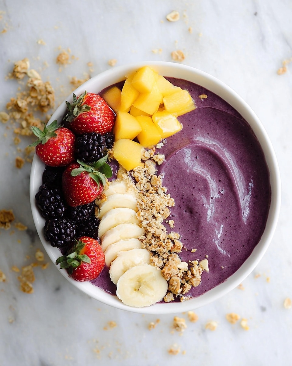 A white bowl contains a thick, smooth, dark purple smoothie as the base layer. On top, there are five white banana slices arranged in a curved line on the right side, several thin, bright yellow mango strips placed near the top center, and a cluster of three bright red strawberries with green stems on the left. Below the strawberries, there are five shiny blackberries. Light brown granola with a crumbly texture is sprinkled mostly on the left side and partially in the middle, along with small seeds scattered over the smoothie and toppings. The bowl sits on a white marbled textured surface with a few granola pieces scattered around. Photo taken with an iphone --ar 4:5 --v 7