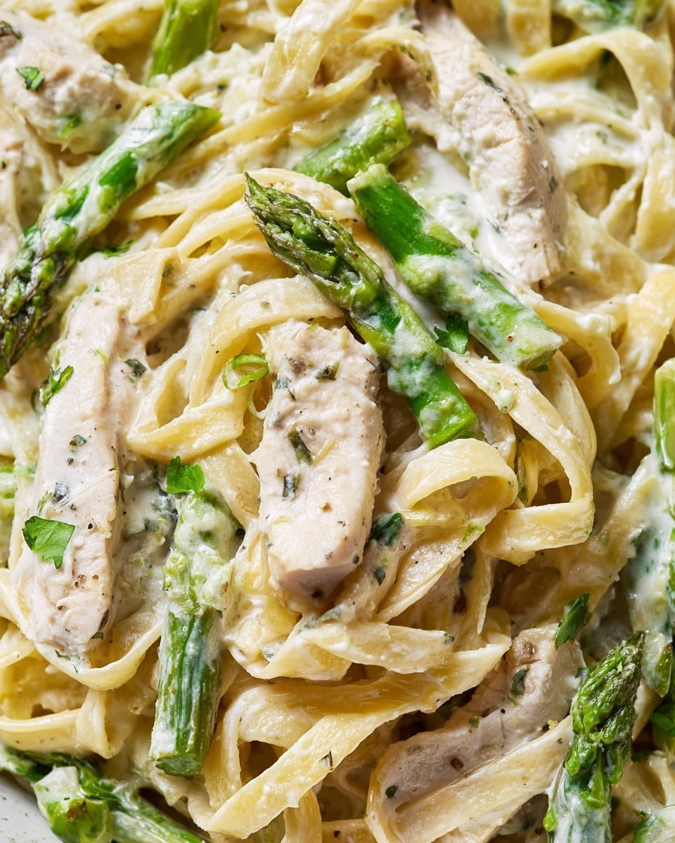 A close-up view of a pan filled with creamy fettuccine pasta mixed with light brown grilled chicken strips and bright green asparagus pieces. The fettuccine noodles are coated in a smooth, white sauce with visible black pepper specks, creating a rich texture. Bright green asparagus spears and tender chicken slices are spread evenly across the top and throughout the pasta. A wooden spoon rests in the pan lifting some asparagus and pasta, with part of a woman's hand holding it. Next to the pan, a piece of crusty bread lies on a white marbled surface. photo taken with an iphone --ar 4:5 --v 7