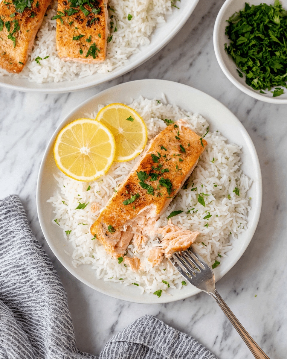 The image shows a white round plate with one large layer of cooked white rice that is fluffy and soft. On top, slightly off center, lies a single piece of grilled salmon, with a golden-brown crust on the outside and a moist, flaky pink inside that is being lifted by a silver fork near the bottom edge. Small green parsley leaves are sprinkled over the salmon and rice. On the left side of the salmon, two small lemon wedges with bright yellow skin and juicy flesh rest directly on the rice. In the background, there is a larger white bowl filled with two more grilled salmon pieces resting on white rice. To the right, there is a small white bowl filled with fresh chopped green herbs. The whole scene is set on a white marbled surface, with a folded grey and white striped cloth napkin near the bottom right corner. photo taken with an iphone --ar 4:5 --v 7