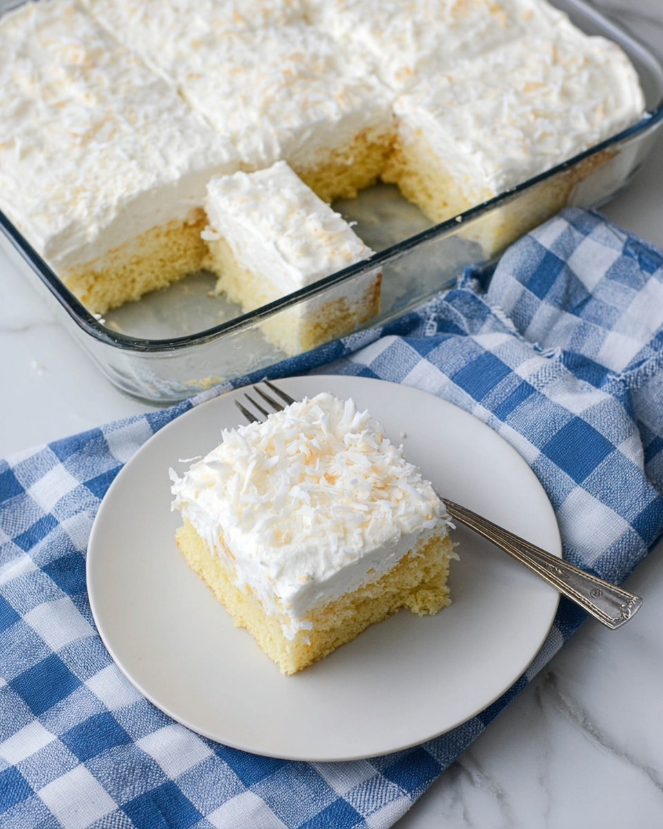 The image shows a close-up of a square white cake dish with a light yellow sponge cake at the bottom, topped with a thick layer of white creamy frosting. The frosting layer is smooth and evenly spread, covered with scattered white shredded coconut. One slice has been removed, revealing the fluffy cake texture inside and crumbs on the white marbled surface below. Photo taken with an iphone --ar 4:5 --v 7