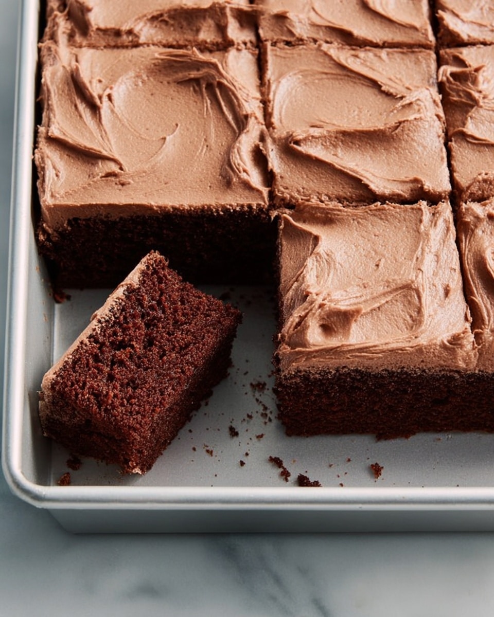 A single square piece of chocolate cake sits on a white plate, showing two thick layers: the bottom layer is a dark brown, moist and crumbly chocolate cake, and the top layer is a lighter brown, smooth and creamy chocolate frosting with gentle swirls on its surface. Small crumbs are scattered around the cake on the plate. The plate rests on a white marbled textured surface, with a white napkin and a silver fork partially visible next to it. Photo taken with an iphone --ar 4:5 --v 7