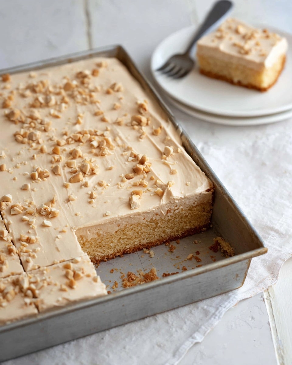 A square slice of two-layer peanut butter dessert sits on a white plate. The bottom layer is thick and light golden brown with a soft, crumbly texture. The top layer is a smooth, creamy light tan peanut butter frosting spread evenly and sprinkled with small, roughly chopped peanuts. There is a bite taken from one corner of the slice, showing the soft crumb structure of the bottom layer. A silver fork lies on the plate with some crumbs around it. In the background, there is a wooden bowl filled with peanuts and a large baking pan with more of the dessert, all placed on a white marbled surface. photo taken with an iphone --ar 4:5 --v 7