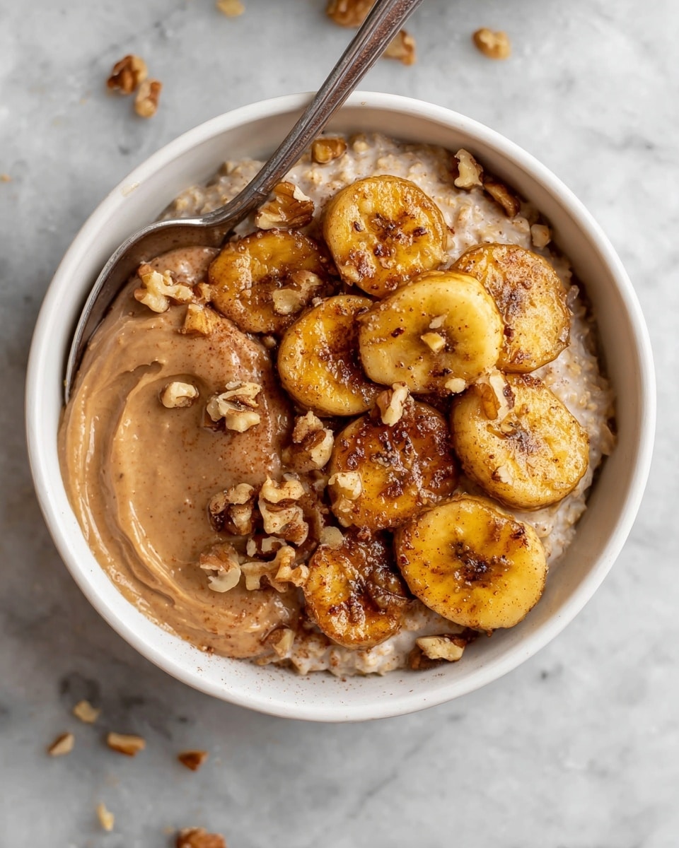 A white bowl filled with creamy oatmeal as the base layer, topped with a smooth spread of light brown nut butter on one side, and golden-brown caramelized banana slices arranged in a neat cluster on the other side. Small chunks of crushed walnuts are sprinkled over the bananas and spread lightly on the oatmeal’s surface, adding texture. A silver spoon rests inside the bowl, partially submerged in the oatmeal. The bowl is placed on a white marbled surface, alongside small white bowls containing walnut pieces and a white jug with dark syrup visible inside. photo taken with an iphone --ar 4:5 --v 7