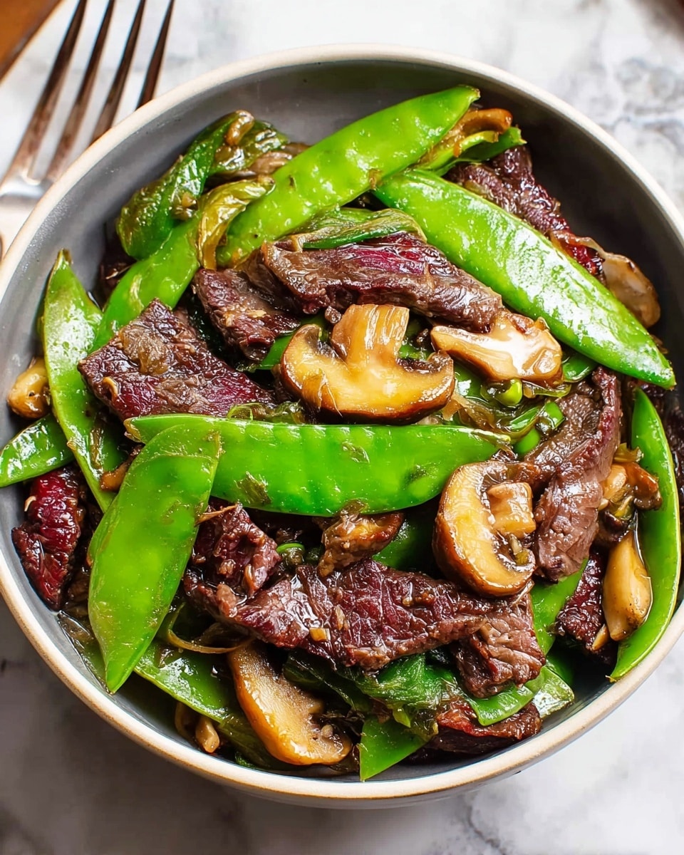 A white bowl filled with a layer of cooked white rice at the bottom, topped with a colorful stir-fry of dark brown beef slices, bright green snow peas, and golden brown sautéed mushrooms. The stir-fry is shiny with sauce, and the vegetables and meat are mixed evenly across the rice. The bowl sits on a white marbled surface, with a silver fork on the left side and a red cup in the background. photo taken with an iphone --ar 4:5 --v 7