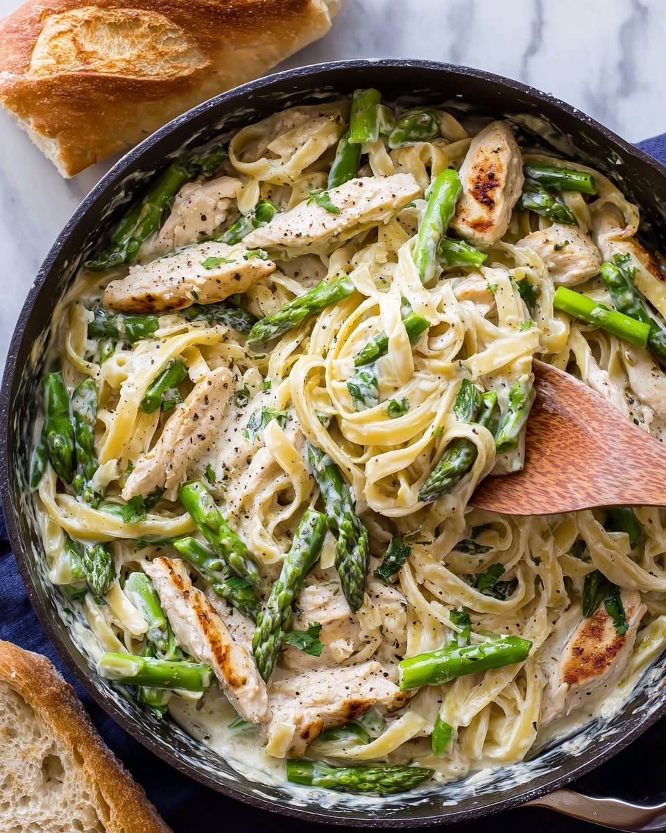 This close-up image shows creamy pasta with three main visible layers: the base layer of smooth, light beige fettuccine noodles, twisted and soft; the middle layer of white chicken strips with a slightly browned texture and small herbs on top, scattered among the noodles; and the top layer featuring bright green asparagus pieces coated in creamy white sauce, along with small green herb pieces sprinkled over the dish. The dish is photographed on a white marbled background. photo taken with an iphone --ar 4:5 --v 7