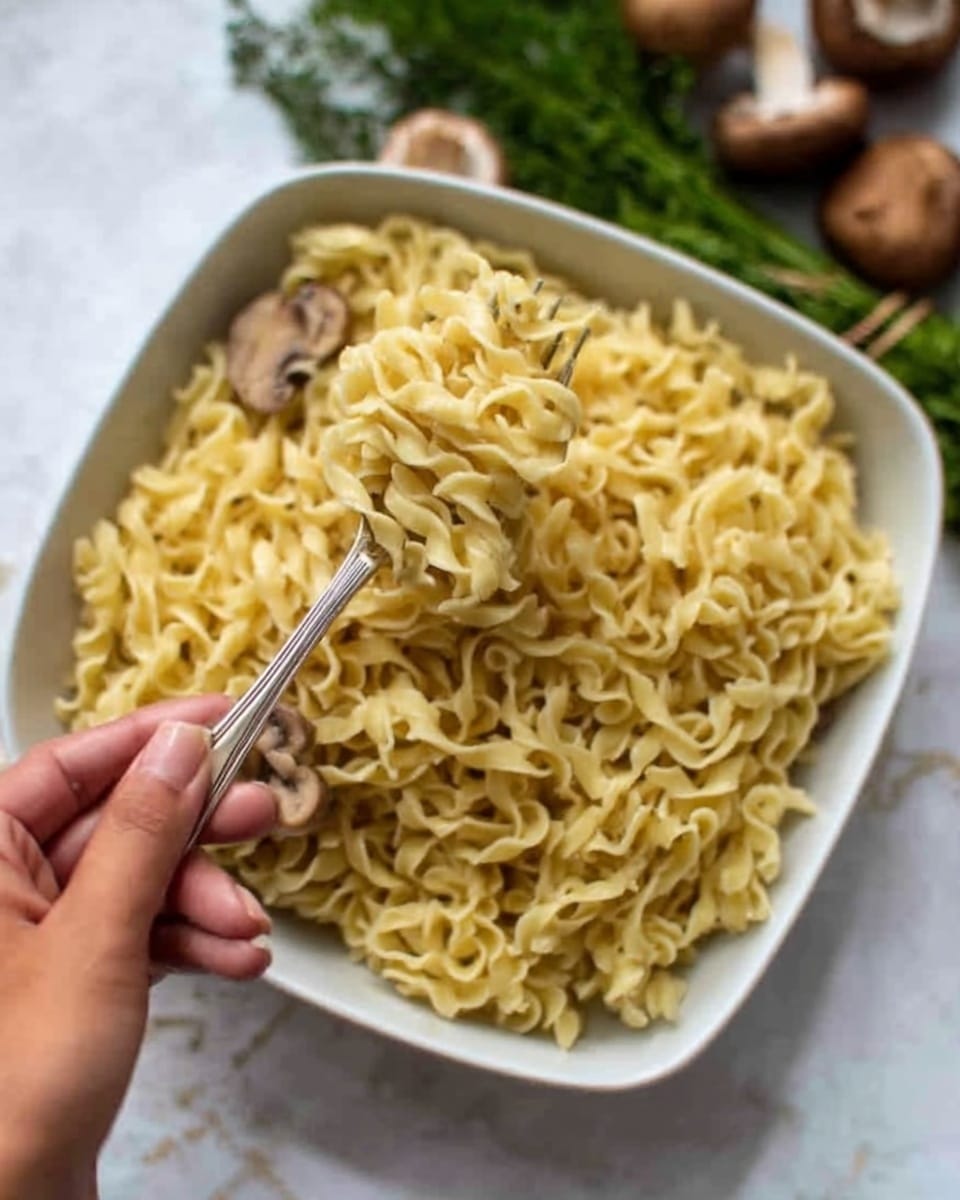 The image shows a white plate with three sections of food placed on a white marbled surface. On the left side of the plate, there is a large serving of buttered egg noodles, light yellow in color with a soft and slightly shiny texture. In the middle, there is a neat row of steamed green beans, long and slender with a bright green color and smooth texture. On the right side, there are two pieces of crispy golden-brown roasted chicken thighs with a textured, slightly wrinkled skin. A woman's hand holding a fork is reaching towards the noodles, lifting a forkful of them. Behind the plate, there is a white bowl filled with more egg noodles. Photo taken with an iphone --ar 4:5 --v 7
