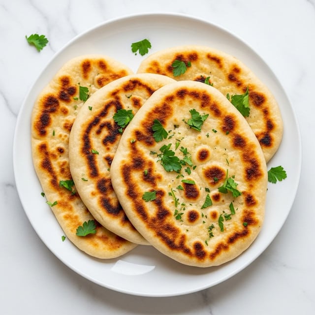 The image shows three pieces of naan bread stacked slightly on top of each other on a white plate. The naan is golden with brown spots from cooking, giving it a soft and slightly crispy texture. Small green parsley leaves are scattered on top of the naan and the plate, adding a fresh, colorful touch. The plate sits on a white marbled surface that adds a clean and simple background to the scene. photo taken with an iphone --ar 4:5 --v 7