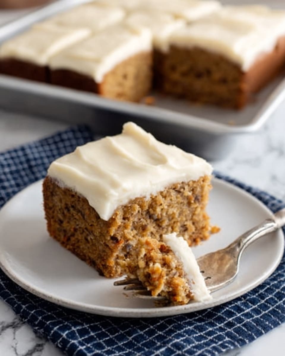 The image shows a square piece of moist carrot cake on a white plate, topped with a thick, smooth layer of cream cheese frosting that is off-white in color. The cake looks dense and has visible small bits of carrot and nuts, giving it a slightly textured and speckled brown appearance. A silver fork with a piece of cake on its tip is placed on the plate, angled toward the cake. In the background, there is a larger tray of the same carrot cake with multiple slices. The plate is set on a dark blue cloth with a grid pattern, and the surface beneath has a white marbled texture. Photo taken with an iphone --ar 4:5 --v 7
