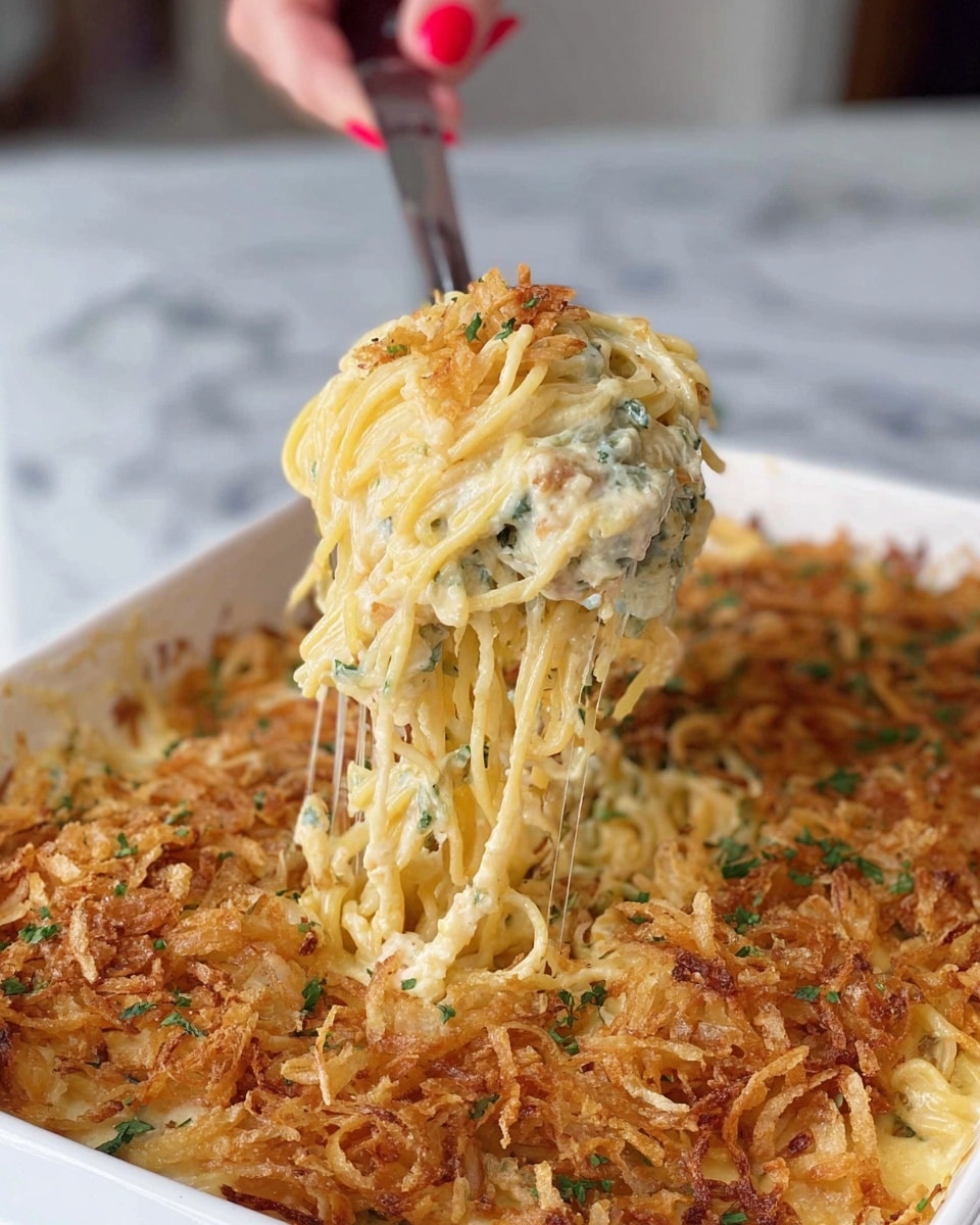A white rectangular baking dish with red handles holds a creamy baked casserole with multiple layers visible through its top. The bottom layer is made of pale yellow noodles mixed with green leafy bits, followed by a thick layer of melted white and light yellow cheese that has a soft, bubbling texture. The top layer is a spread of golden-brown crispy fried onions, adding a crunchy texture and a darker color contrast to the dish. The baking dish rests on a white marbled surface. photo taken with an iphone --ar 4:5 --v 7