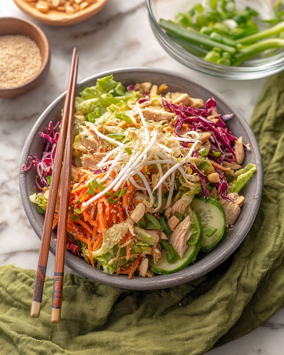 A close-up view of a colorful Asian chicken salad in a white bowl, showing three main layers: a base of green leafy vegetables and chopped cucumbers mixed with thin strips of purple cabbage and orange carrots; a middle layer of light beige shredded chicken pieces coated in a glossy sauce along with crunchy peanuts; and a top layer sprinkled with white sesame seeds and small bits of green herbs, all lifted slightly by an ornate silver fork in the center. The textures contrast between crispy vegetables, tender chicken, and crunchy nuts. The bowl sits on a white marbled surface. Photo taken with an iphone --ar 4:5 --v 7