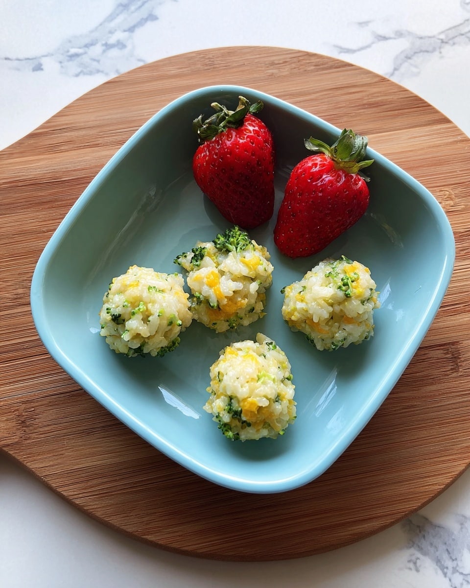 In a white square bowl, there are five small, round rice balls mixed with bits of green broccoli and orange cheese, spaced out evenly across the bottom. Two large red strawberries with green tops are placed side by side at the upper part of the bowl. The bowl is set on a round wooden board over a white marbled surface, creating a clean and simple setting. photo taken with an iphone --ar 4:5 --v 7