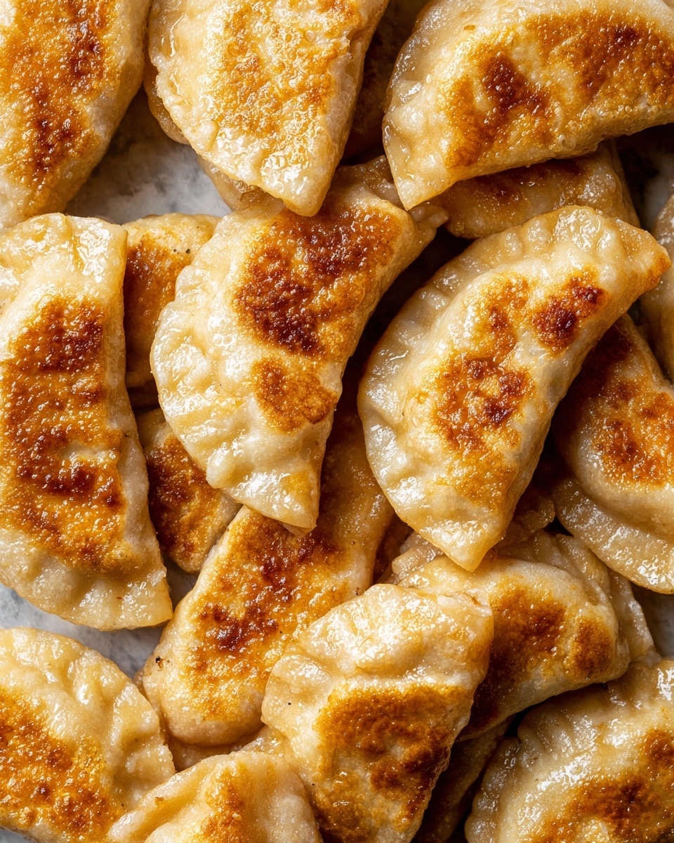 The image shows many golden brown pierogi close together, with a crispy outer layer that has a textured, slightly bubbly surface. Each pierogi is half-moon shaped with pinched edges forming a crimped seam. The top is browned in spots, showing a mix of light to dark golden tones. They look slightly oily, giving a shiny look in some areas. The pierogi fill the whole frame, resting on a white marbled texture barely visible in the background. photo taken with an iphone --ar 4:5 --v 7