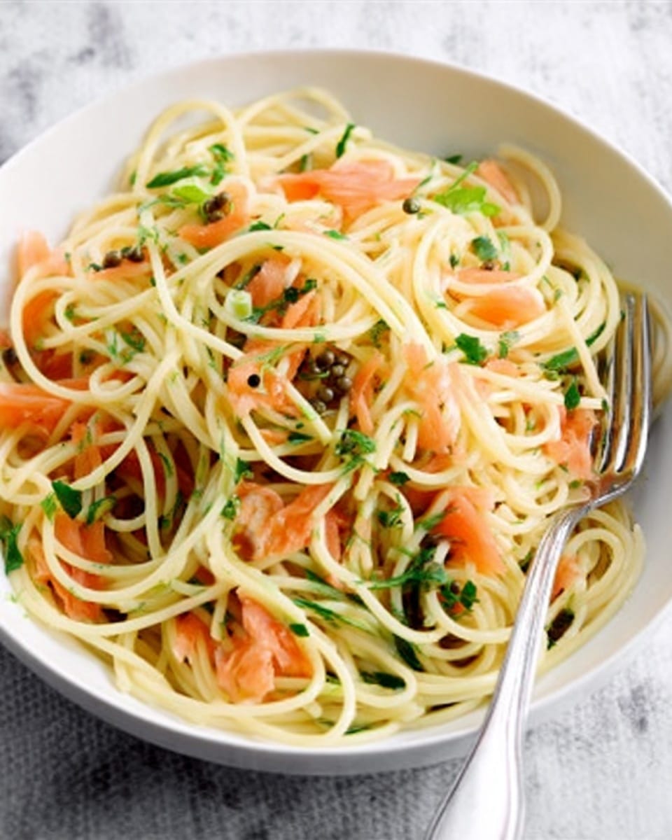 A white plate holds a serving of spaghetti pasta mixed with light orange smoked salmon pieces and dark green spinach leaves, with a few small capers scattered throughout. The pasta strands are creamy yellow, soft, and slightly twisted, interwoven with the other ingredients. A silver fork rests on the right edge of the plate, with some pasta delicately twirled around its tines. The plate is placed on a white marbled surface with a dark round wooden board underneath and a navy blue cloth partially visible. Photo taken with an iphone --ar 4:5 --v 7