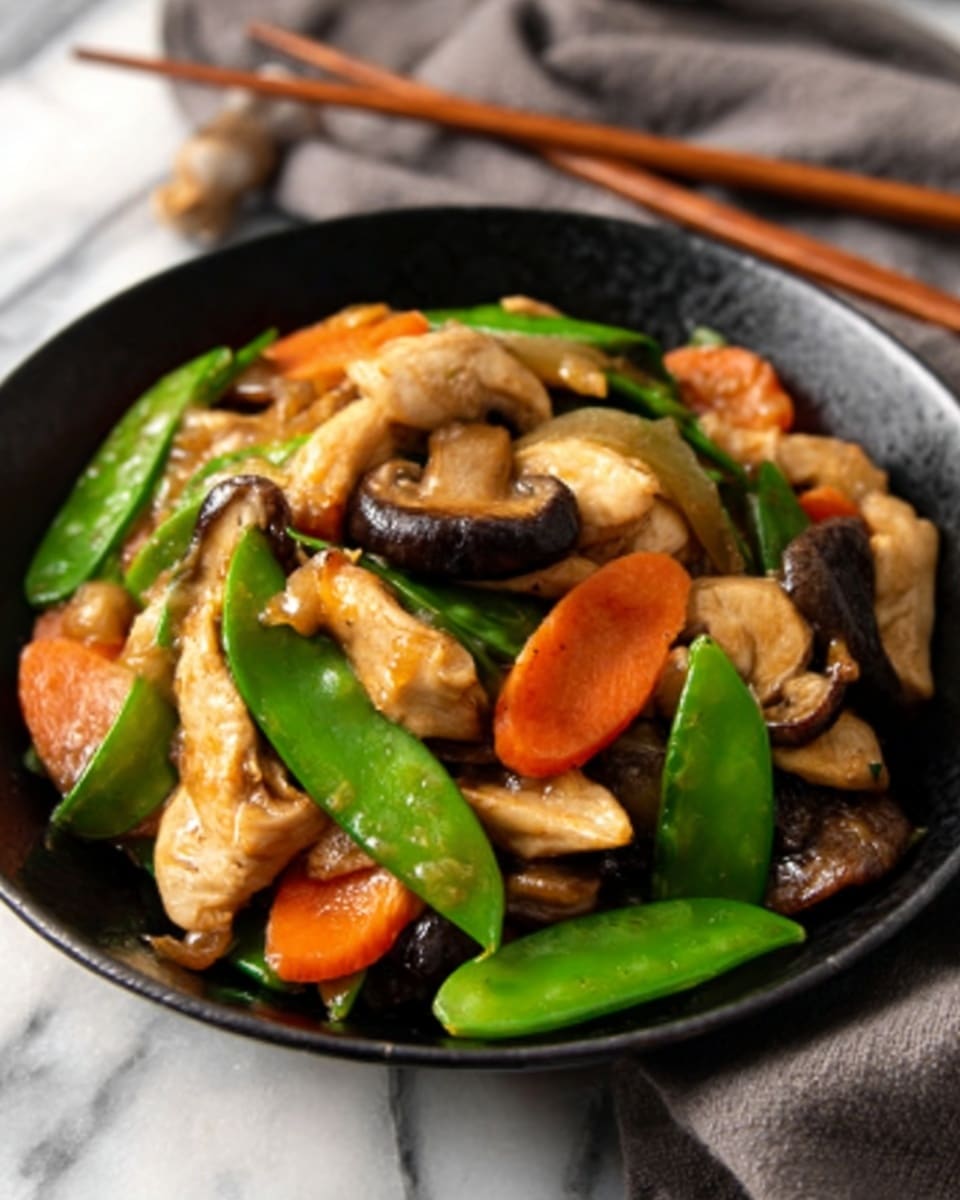 A close-up of a black bowl filled with a colorful stir-fry dish. The dish has multiple layers: at the bottom, there are slices of light brown cooked chicken, mixed with light green snap peas and orange carrot slices scattered on top. There are also pieces of beige mushrooms and some dark brown shiitake mushrooms, all coated with a shiny sauce. The bowl rests on a white marbled surface, and a pair of wooden chopsticks and a grey cloth are visible in the background. photo taken with an iphone --ar 4:5 --v 7